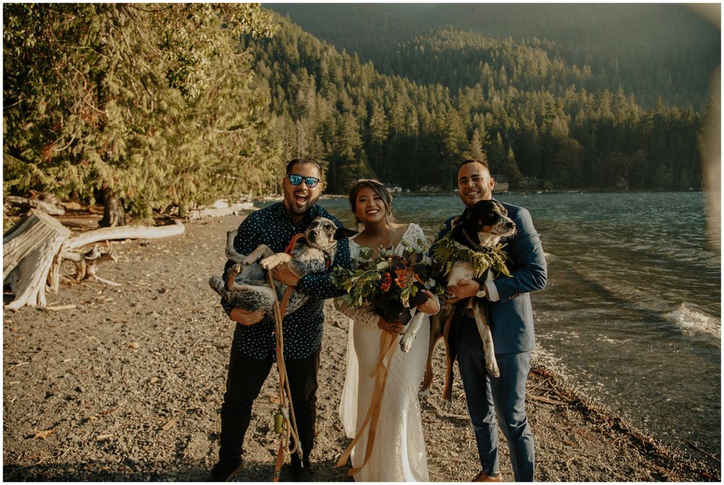 couple posing with pet dogs in front of lake