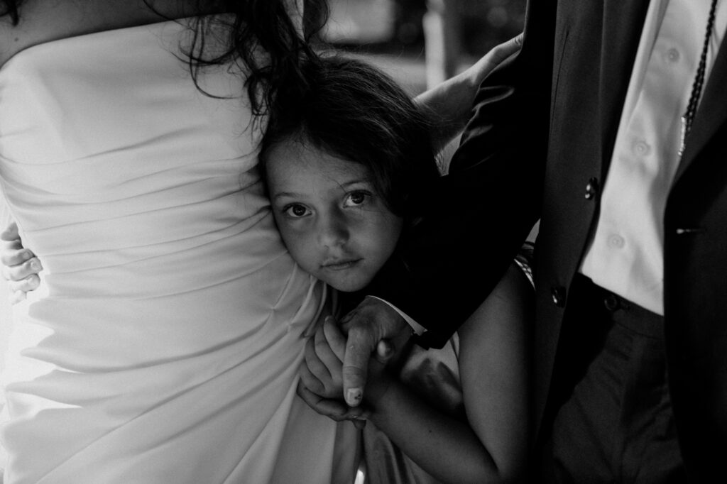 daughter in between bride and groom hugging on wedding day