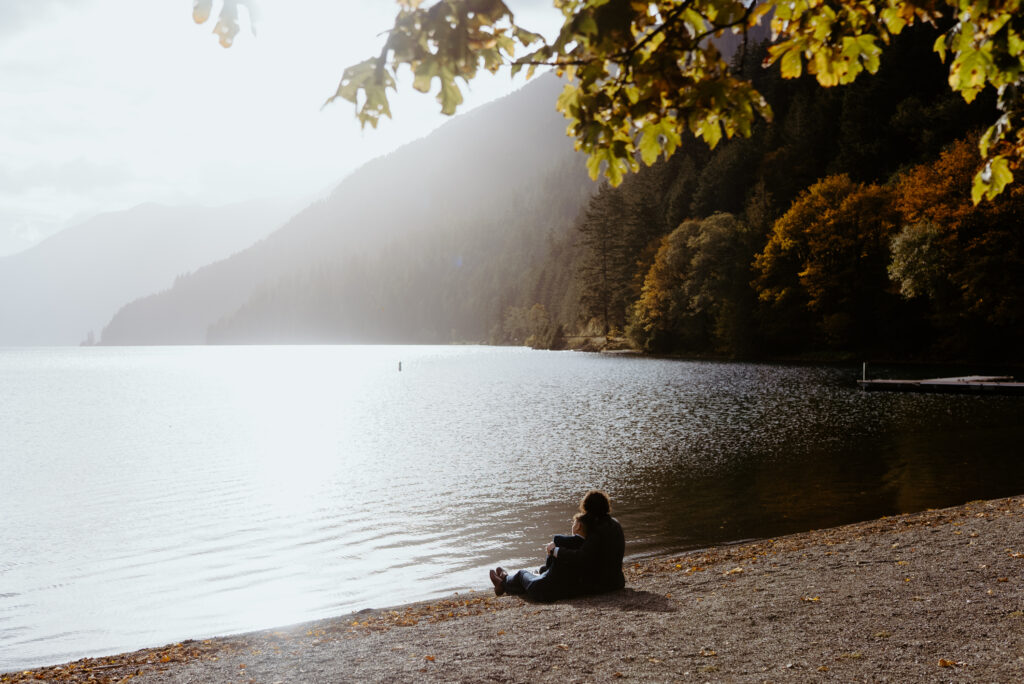 non binary couple sitting in the view of lake crescent from the north shore dock